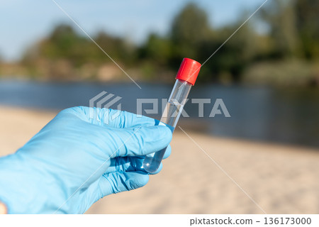 Hand in blue medical glove with test tube. Concept of taking water from river beach for testing 136173000