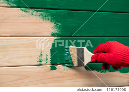 Man applying protective ink varnish with brush to wooden wall. Painting building to protect it from moisture and make more beautiful Man applying protective ink varnish with brush to wooden wall. Painting building to protect it from moisture and make more beautiful 136173008