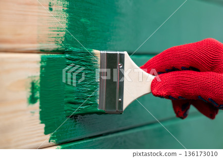 Painting wall in green color. Applying dye to wooden wall of a house with brush Painting wall in green color. Applying dye to wooden wall of a house with brush 136173010