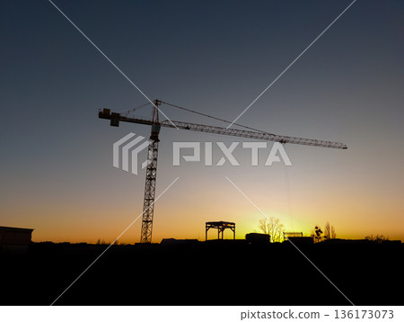 Construction crane silhouette at sunset over urban skyline 136173073