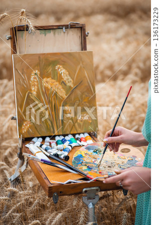 Hands of an artist taking some oil ink, almost finished painting of spikelets on the background. Drawing process Hands of an artist taking some oil ink, almost finished painting of spikelets on the background. Drawing process 136173229
