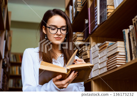 Concentrated female student working in the library alone, studying many books to find information for the presentation. University student in the library 136173232