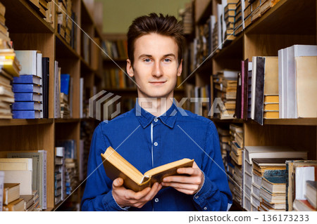 Male student finding information in books, preparing for exams. Portrait of young student in the library with a book in his hands 136173233
