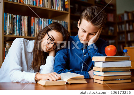 Two bored students in the library. Male and female students feeling sick and tired of preparation for final exams as they read many books lately 136173236