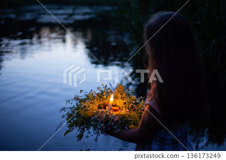 Girl with ritual wreath going to the river late in the evening. Ivan Kupala celebration, ritual wreath with burning candle 136173249