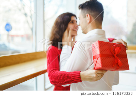 Man gives to his woman a gift box with red ribbon. A loving couple celebrating Valentine's Day. Man gives to his woman a gift box with red ribbon. A loving couple celebrating Valentine's Day. 136173323