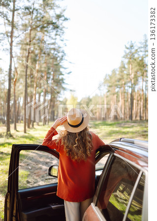 Young woman enjoying a sunny day by her car in forest setting during the afternoon. Summer trip Young woman enjoying a sunny day by her car in forest setting during the afternoon. Summer trip 136173382