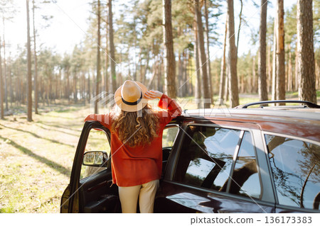 Young woman enjoying a sunny day by her car in forest setting during the afternoon. Summer trip Young woman enjoying a sunny day by her car in forest setting during the afternoon. Summer trip 136173383