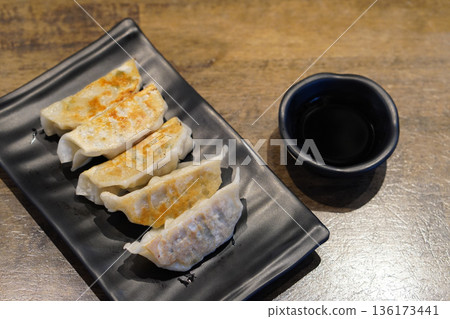 five pieces of gyoza in a black ceramic plate and sauce in a black ceramic cup on wooden floor background, food, snack, copy space 136173441