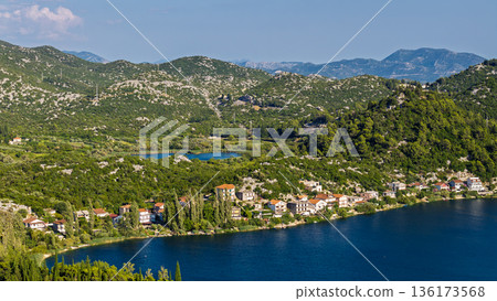 Aerial view of Dalmatian karst lake village in Croatia with waterfront houses green hills and calm water 136173568