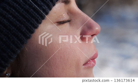 Detail view of attractive female face illuminating by warm rays of sun at winter day. Calm facial expression of young woman. Tranquil sight with green eyes of beautiful girl. Close up 136173614