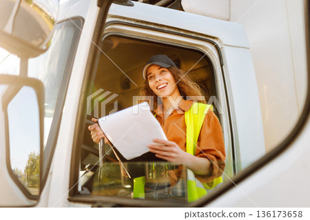 Portrait of beautiful young woman professional truck driver checking shipment list on a -parking lot Portrait of beautiful young woman professional truck driver checking shipment list on a -parking lot 136173658