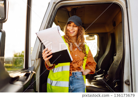 Portrait of beautiful young woman professional truck driver checking shipment list on a -parking lot Portrait of beautiful young woman professional truck driver checking shipment list on a -parking lot 136173679