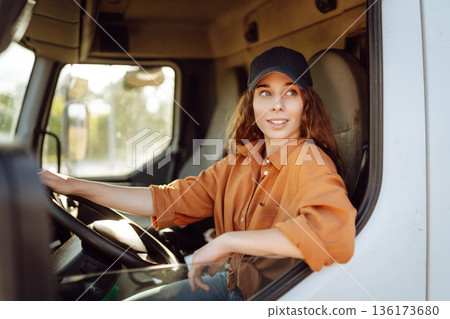 Portrait of beautiful young woman professional truck driver driving a big truck. Inside of vehicle Portrait of beautiful young woman professional truck driver driving a big truck. Inside of vehicle 136173680