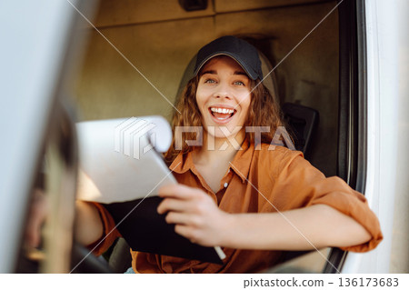 Portrait of beautiful young woman professional truck driver driving a big truck. Inside of vehicle Portrait of beautiful young woman professional truck driver driving a big truck. Inside of vehicle 136173683