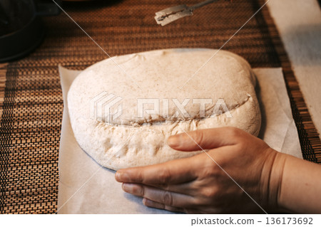 Scoring raw homemade bread dough with a special tool Scoring raw homemade bread dough with a special tool 136173692
