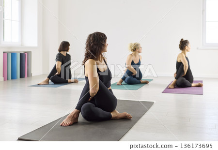 Women in yoga class performing seated spinal twist for flexibility and calm 136173695