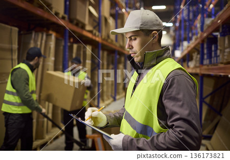 Warehouse inventory control with worker writing checklist as boxes are moved Warehouse inventory control with worker writing checklist as boxes are moved 136173821