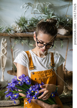 Calm florist woman surrounded by plants holding bouquet of irises flowers. Owner flower store 136173826
