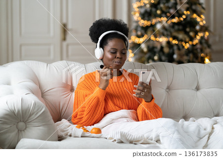 African woman spend christmas morning at home in living room with xmas tree read sms in smartphone 136173835