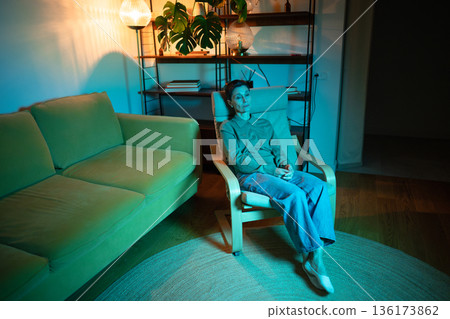 Senior woman sit in chair at home in rgb light looking with apathy, sadness and mental exhaustion. Senior woman sit in chair at home in rgb light looking with apathy, sadness and mental exhaustion. 136173862
