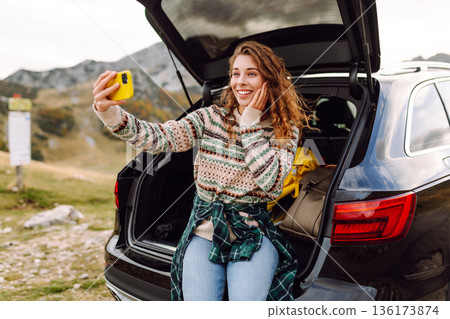 Young traveler woman taking a selfie by her car in the mountains during sunset. Lifestyle, travel 136173874