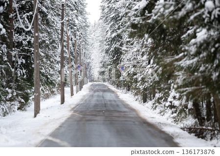 Countryside roadway with signs surrounded by spruce trees forest covered in snow on cold winter day. Countryside roadway with signs surrounded by spruce trees forest covered in snow on cold winter day. 136173876
