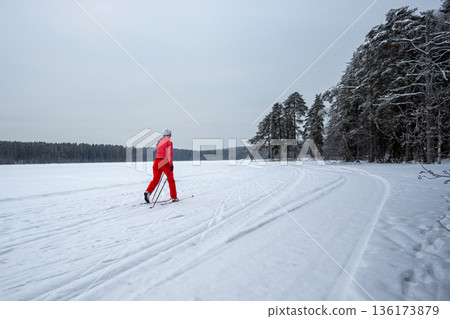Woman keeping physical activity in winter, enjoying skiing on frosty day at frozen lake outdoors. 136173879