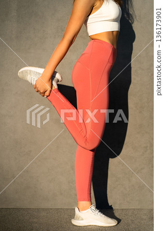 Sporty woman in pink sportswear stretch knee muscles, hold leg tightly back, unrecognizable closeup 136173901