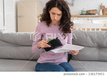 Sad young girl holding last cash money feeling anxiety about debt or bankruptcy, sitting at home. 136173951