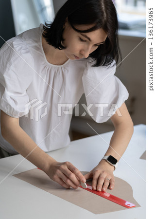Female tailor use ruler to sketch pattern cloth to cut material. Designer or seamstress in atelier 136173965