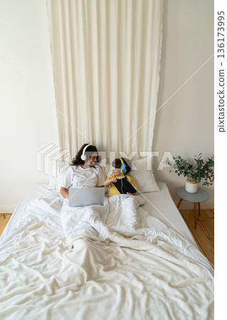 Mom and Son work and study lying together in bed using laptop computer and digital tablet in bedroom Mom and Son work and study lying together in bed using laptop computer and digital tablet in bedroom 136173995