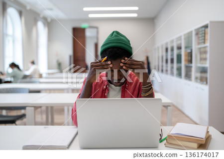 Exhausted mixed race student man touch head feel migraine after laptop study in university library Exhausted mixed race student man touch head feel migraine after laptop study in university library 136174017