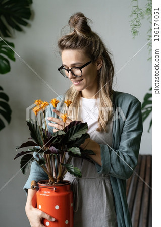 Woman florist holding flowering calathea plant in old red milk can standing in home garden Woman florist holding flowering calathea plant in old red milk can standing in home garden 136174051