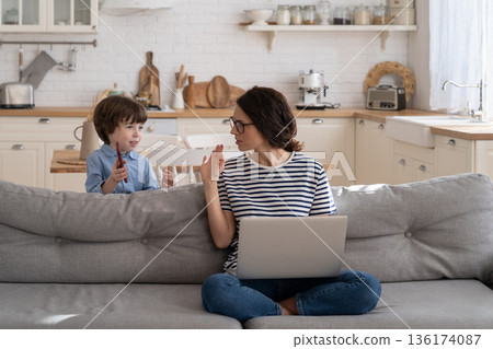 Freelancer mom working on laptop at home during lockdown, noisy child distracts asking attention. Freelancer mom working on laptop at home during lockdown, noisy child distracts asking attention. 136174087