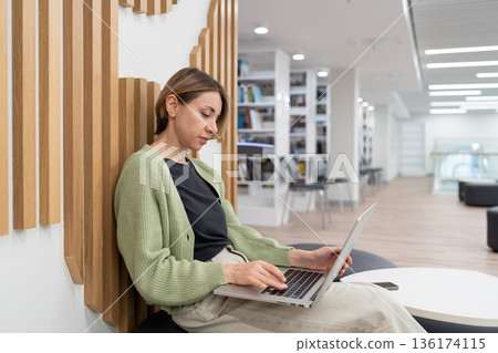 Focused woman freelance writer working on laptop in library. Freelancing after 40 136174115