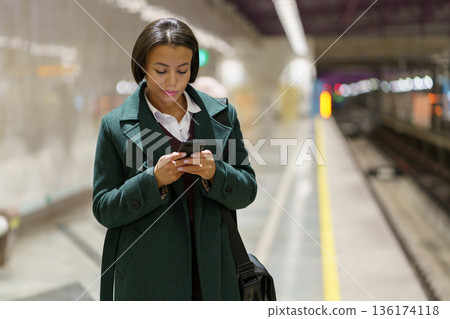 Nomophobia. African american businesswoman surfing wireless internet on smartphone at subway Nomophobia. African american businesswoman surfing wireless internet on smartphone at subway 136174118