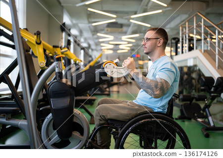 Focused disabled man in wheelchair using upper body ergometer for recovery after spinal injury. Focused disabled man in wheelchair using upper body ergometer for recovery after spinal injury. 136174126