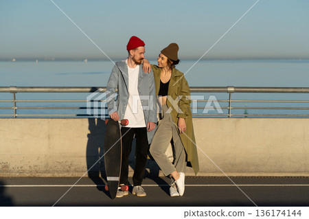 Happy couple of lovers hipsters with longboard on bridge in sunshine smiling wearing stylish clothes Happy couple of lovers hipsters with longboard on bridge in sunshine smiling wearing stylish clothes 136174144