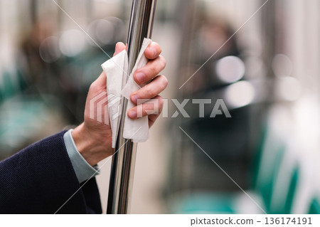 Hand holds handrail in public transport through a napkin to protect from contact with viruses, germs Hand holds handrail in public transport through a napkin to protect from contact with viruses, germs 136174191