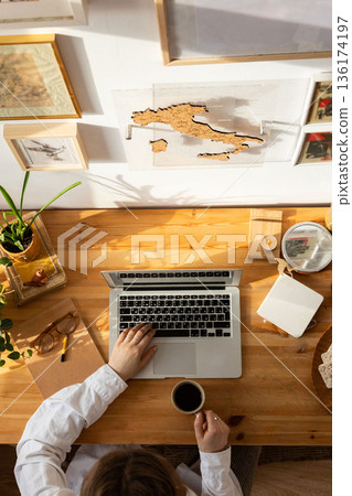 Wooden desktop top view, woman designer hands using laptop and holding a cup of coffee.Freelancer working place.Work from home. Wooden desktop top view, woman designer hands using laptop and holding a cup of coffee.Freelancer working place.Work from home. 136174197
