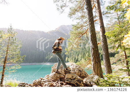 Young woman traveler enjoys fresh air and a beautiful view of the lake and mountains. Active life 136174226