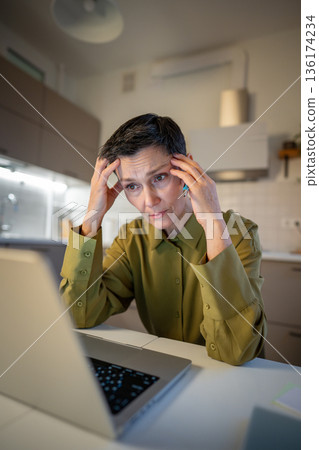 Senior businesswoman with migraine staring at laptop screen, dealing with heavy stress at work. 136174234