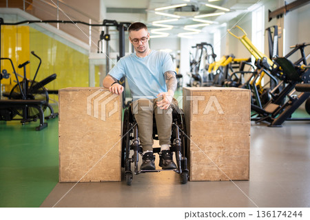 Focused disabled man athlete in wheelchair getting motivation in gym for long rehabilitation period. Focused disabled man athlete in wheelchair getting motivation in gym for long rehabilitation period. 136174244