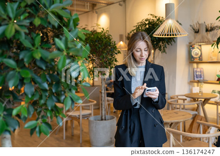 Positive successful business woman restaurant manager texting on smartphone during work break. Positive successful business woman restaurant manager texting on smartphone during work break. 136174247