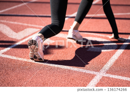 Rear view of woman jogger on running track getting ready to start run.. 136174266