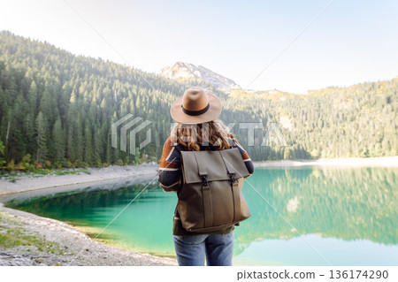 Young woman traveler enjoys fresh air and a beautiful view of the lake and mountains. Active life 136174290