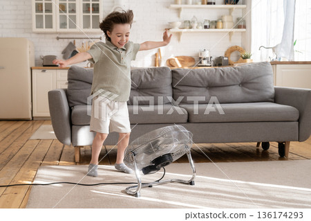 Small boy play with strong wind blow from ventilator or retro fan at home in cozy living room alone Small boy play with strong wind blow from ventilator or retro fan at home in cozy living room alone 136174293
