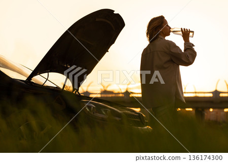 woman drinking water, waiting for assistance near her car broken down with open bonnet at sunset woman drinking water, waiting for assistance near her car broken down with open bonnet at sunset 136174300