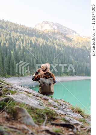 Young woman traveler enjoys fresh air and a beautiful view of the lake and mountains. Active life 136174309